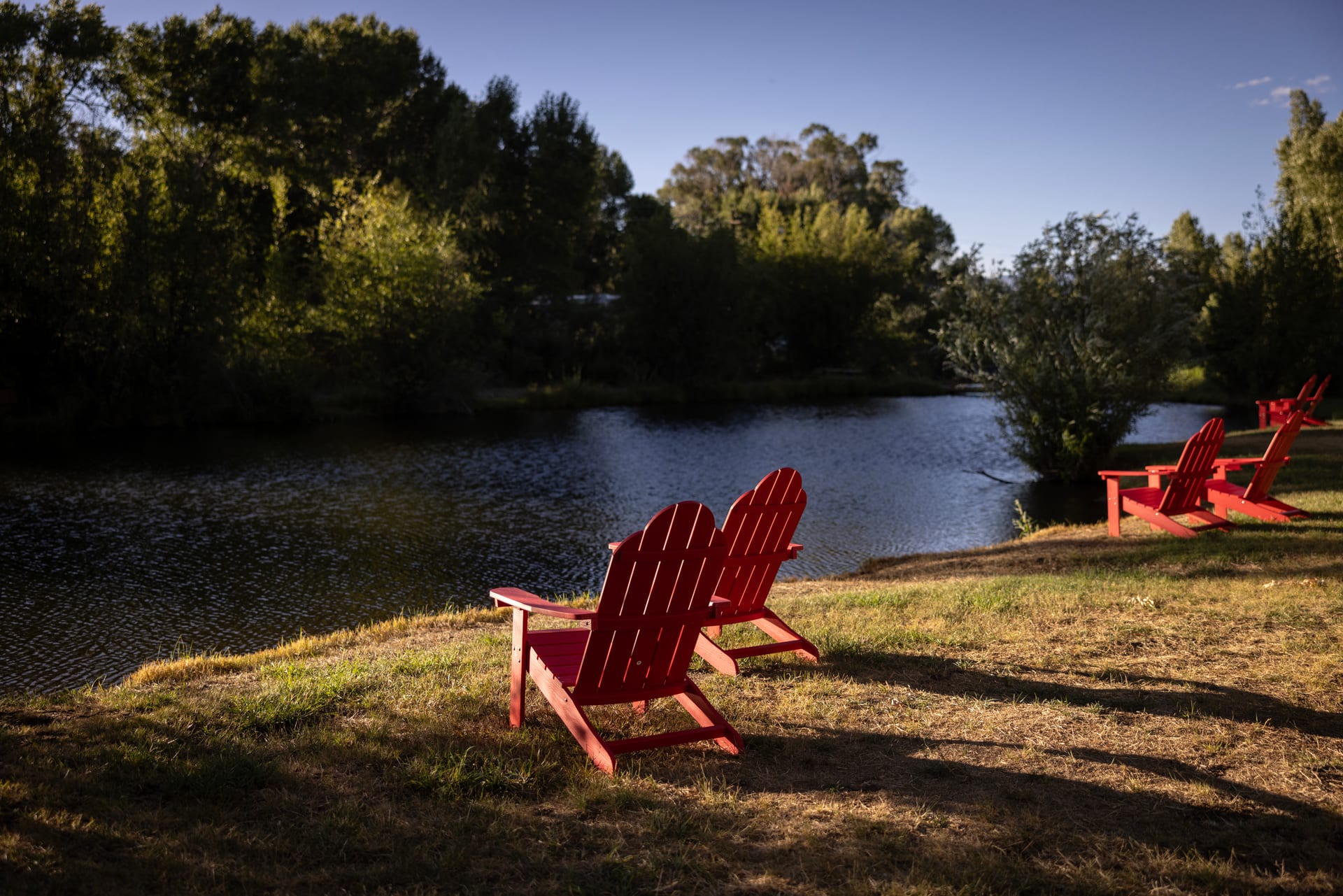 Red adirondack chairs on the pond bank at golden hour at Outdoorsy Bayfield